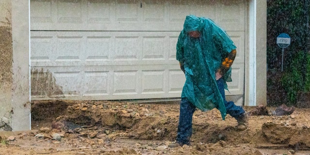 A man in heavy rain jumps over mudslide and rushing water from hillside in front of his home on the 3700 block of North Fredonia Drive on Tuesday, Jan. 10, 2023, in Studio City, California. 