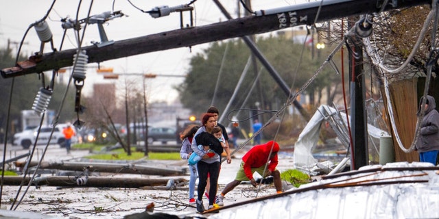 People cross under downed power lines where a tornado was reported to pass along Mickey Gilley Boulevard near Fairmont Parkway, Tuesday, Jan. 24, 2023, in Pasadena, Texas. 
