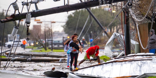 People cross under downed power lines where a tornado was reported to pass along Mickey Gilley Boulevard near Fairmont Parkway, Tuesday, Jan. 24, 2023, in Pasadena, Texas. 