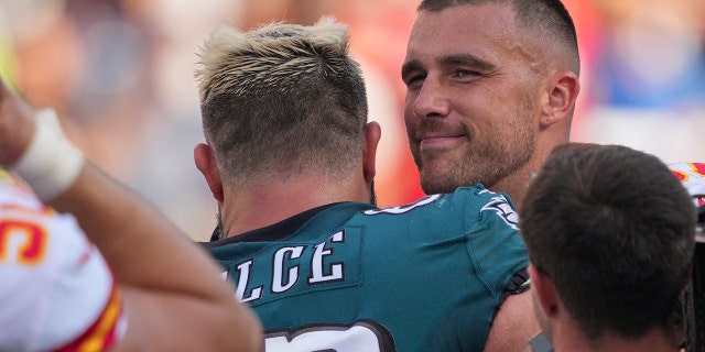 El centro de los Philadelphia Eagles, Jason Kelce, al centro, y el ala cerrada de los Kansas City Chiefs, Travis Kelce, a la derecha, se abrazan durante un partido el 3 de octubre de 2021 en el Lincoln Financial Field de Filadelfia.