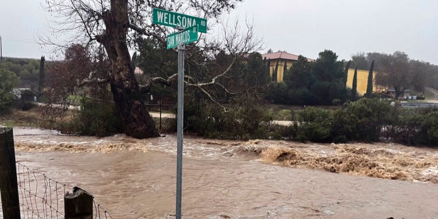 In this photo provided by Neil Collins, floodwaters continue to flow at the intersection of Wellsona and San Marcos Roads near the San Marcos Creek in San Miguel, California, on Monday, Jan. 9, 2023.