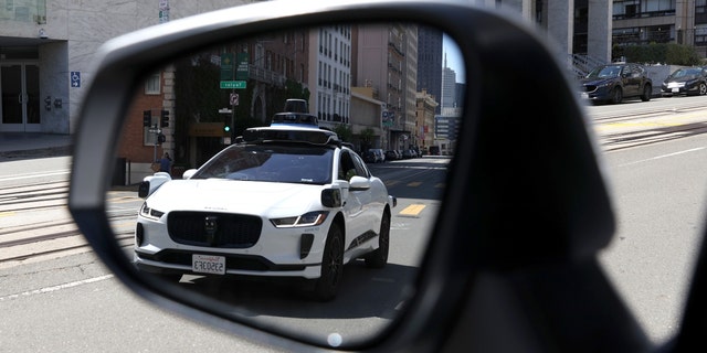 A Waymo self-driving car is reflected in a mirror as it drives down California Street in San Francisco, California, on April 11, 2022. 