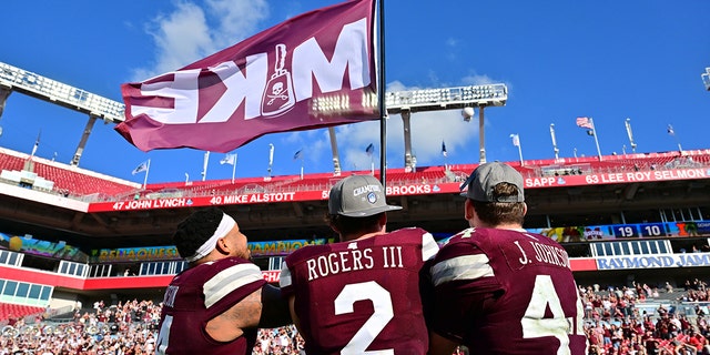Nathaniel Watson #14, Will Rogers III #2 and Jett Johnson #44 of the Mississippi State Bulldogs wave a Mike flag in memory of Mike Leach after defeating the Illinois Fighting Illini 19-10 in the ReliaQuest Bowl at Raymond James Stadium on January 2, 2023 in Tampa, Florida.