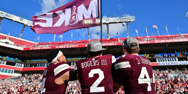 Nathaniel Watson #14, Will Rogers III #2 y Jett Johnson #44 de los Mississippi State Bulldogs ondean una bandera de Mike en memoria de Mike Leach después de derrotar a Illinois Fighting Illini 19-10 en el ReliaQuest Bowl en el Estadio Raymond James el 2 de enero de 2023 en Tampa, Florida.