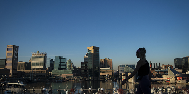 A pedestrian walks past the downtown Baltimore skyline in Federal Hill park in Baltimore on Friday, Nov. 20, 2020. Coronavirus infections continue to rise in the greater Washington region, with more than 5,000 new cases reported on Thursday, a daily record.