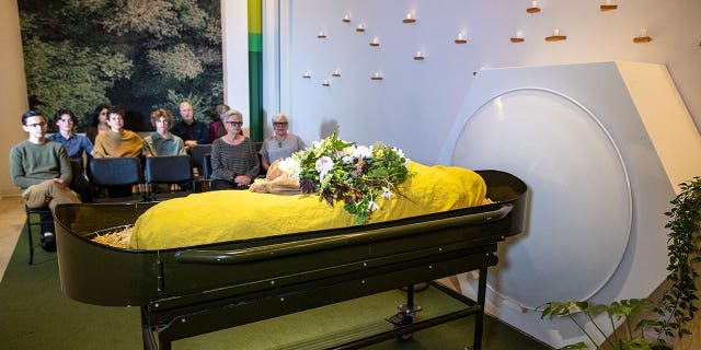 Guests sit in the gathering space looking at a shrouded mannequin in front of the threshold vessel at Recompose, a green funeral home specializing in human composting, also known as natural organic reduction, terramation, or recomposition at Recompose Seattle on October 06, 2022 in Seattle, Washington.