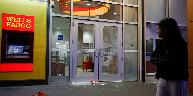 People walk by broken windows at a Wells Fargo branch following a violent protest, late Saturday, Jan. 21, 2023, in Atlanta, in the wake of the death of an environmental activist killed after authorities said the 26-year-old shot a state trooper. 