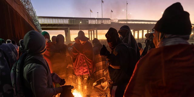 Des immigrants se réchauffent près d'un feu à l'aube après avoir passé une nuit le long de la barrière frontalière américano-mexicaine le 22 décembre 2022 à El Paso, au Texas.