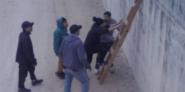 Hidden camera footage capturing illegal immigrants using a makeshift ladder to scale the wall. 