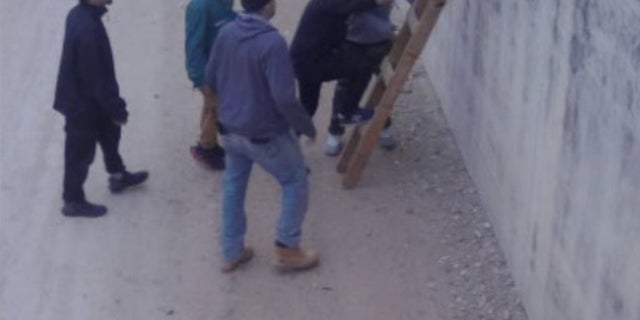 Hidden camera footage capturing illegal immigrants using a makeshift ladder to scale the wall. 