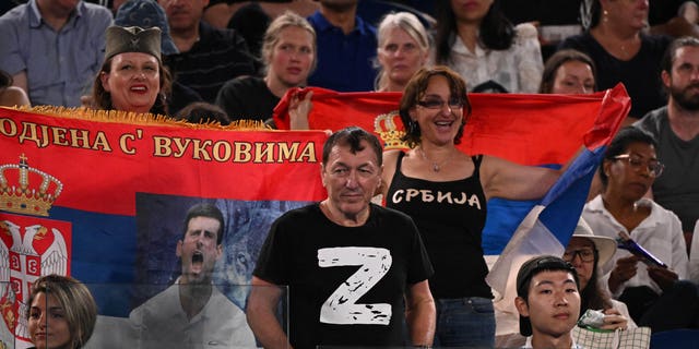 رجل يرتدي واحدة "ض" تي شيرت يظهر مباراة ربع نهائي فردي الرجال بين الصربي نوفاك ديوكوفيتش والروسي أندري روبل ، بجانب المشجعين الذين يرفعون الأعلام الصربية ، في اليوم العاشر من بطولة أستراليا المفتوحة للتنس في ملبورن في 25 يناير 2023. 