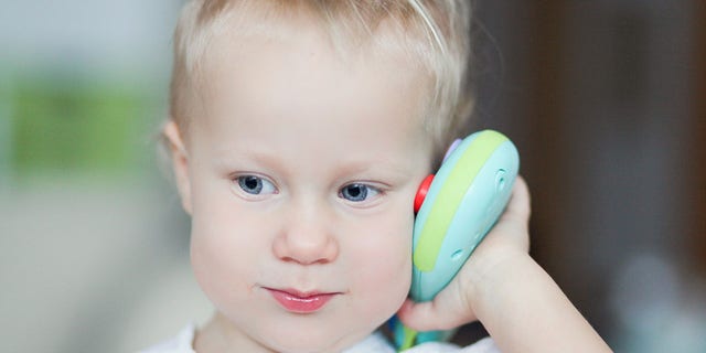 A young child is shown holding a toy (not the one mentioned in the story) to her ear. One TikTok user commented on Ashley Lynn's video, noting, "This world will seriously do anything to corrupt a child's brain. I didn't realize they were literally starting with babies."