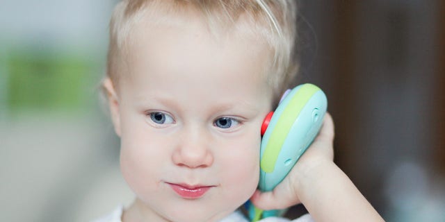 A young child is shown holding a toy (not the one mentioned in the story) to her ear. One TikTok user commented on Ashley Lynn's video, noting, "This world will seriously do anything to corrupt a child's brain. I didn't realize they were literally starting with babies."