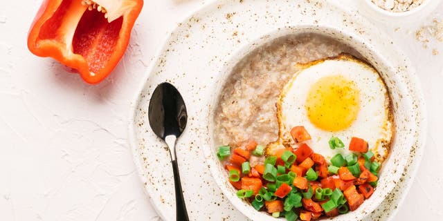 This trendy savory oatmeal bowl includes a fried egg, chopped red bell pepper and scallions.