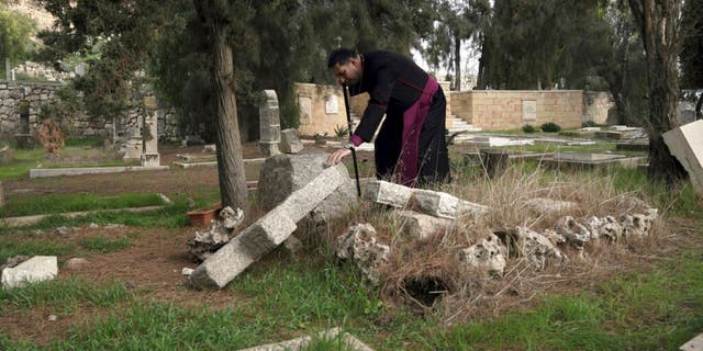 2023 年 1 月 4 日水曜日、エルサレムのシオン山にある歴史的なプロテスタント墓地で、破壊者が 30 以上の墓を冒涜したため、破壊された墓に触れるパレスチナの聖公会司教フッサム ナウム。