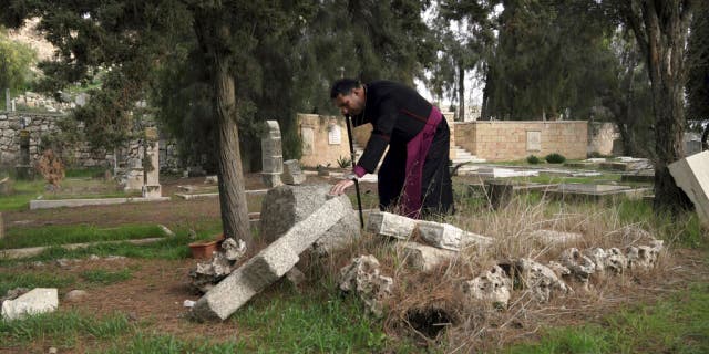 Hosam Naoum, a Palestinian Anglican bishop, touches a damaged grave where vandals desecrated more than 30 graves at a historic Protestant Cemetery on Jerusalem's Mount Zion in Jerusalem, Wednesday, Jan. 4, 2023.