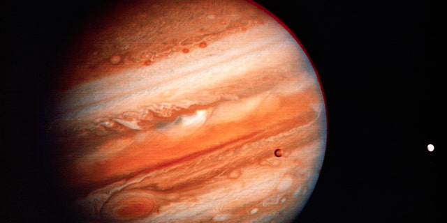 Une vue de Jupiter du début de la mission Voyager 1.  Les deux lunes galiléennes d'Io et d'Europe (de gauche à droite) peuvent également être vues. 