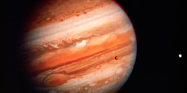 Une vue de Jupiter du début de la mission Voyager 1.  Les deux lunes galiléennes d'Io et d'Europe (de gauche à droite) peuvent également être vues. 