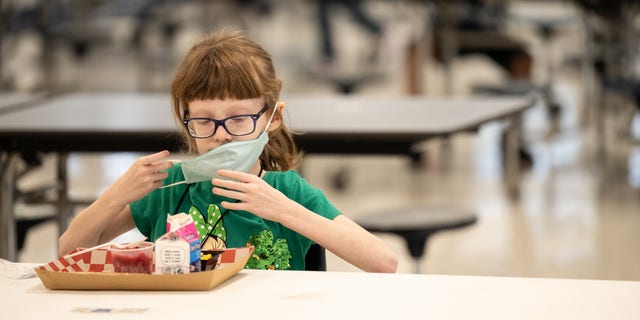 Een kind zet op 17 maart 2021 haar masker weer op na het beëindigen van de lunch aan een tafel met sociale afstand in de cafetaria van de Medora Elementary School in Louisville, Kentucky.