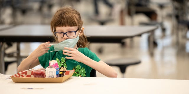 A child puts her mask back on after finishing lunch at a socially distanced table in the cafeteria of Medora Elementary School in Louisville, Kentucky, on March 17, 2021.