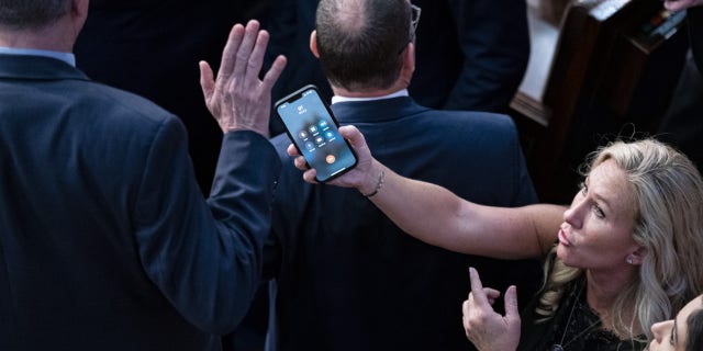 Rep. Marjorie Taylor Greene, a Republican from Georgia, holds her phone with former President Donald Trump on the line, as Rep. Matt Rosendale, a Republican from Montana, waves it off during a meeting of the 118th Congress in the House Chamber at the U.S. Capitol in Washington, D.C., Friday, Jan. 6, 2023.