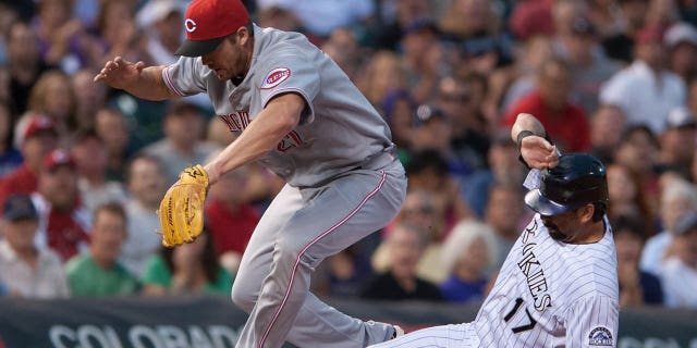 Scott Rolen #27 of the Cincinnati Reds leaps as Todd Helton #17 of the Colorado Rockies slides safely into third base in the sixth inning of a game at Coors Field on July 28, 2012 in Denver, Colorado. The Reds defeated the Rockies 9-7.