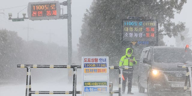 A police officer controls vehicle traffic amid heavy snowfall on Jeju Island, South Korea, on Jan. 24, 2023.