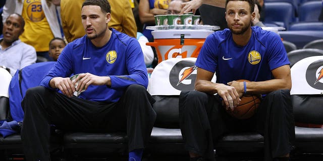 Stephen Curry, a la derecha, y Klay Thompson de los Golden State Warriors se sientan en la banca antes de un partido contra los New Orleans Pelicans en el Smoothie King Center el 4 de diciembre de 2017 en Nueva Orleans.