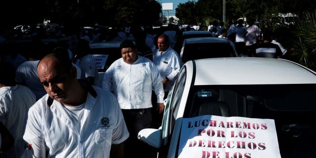 Taxi drivers walk past a sign reading, "We are fighting for the rights of the taxi drivers," during a protest against the regulation of taxi-hailing apps such as Uber in Cancun, Mexico, Jan. 11, 2023.