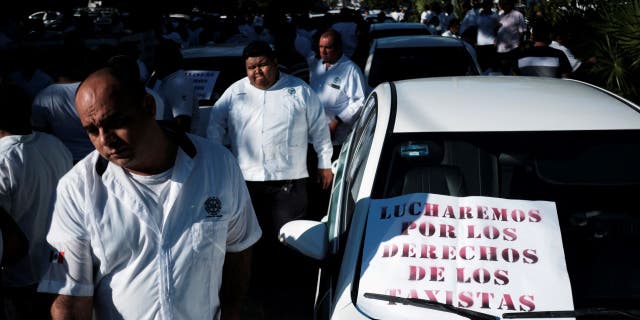 Taxi drivers walk past a sign that reads, 