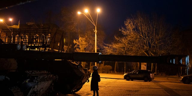 Seorang wanita berdiri di depan pajangan tank dan kendaraan lapis baja Rusia yang hancur di pusat kota Kyiv, Ukraina, Jumat, 20 Januari 2023. (Foto AP/Daniel Cole)