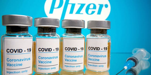 COVID-19 vaccine vials displayed next to a medical syringe is seen in front of a Pfizer logo on Oct. 31, 2020.