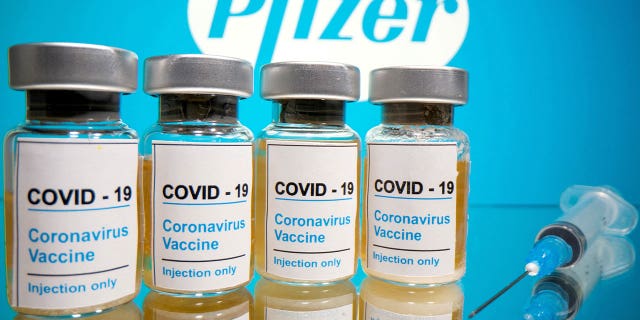 Op 31 oktober 2020 worden injectieflacons met COVID-19-vaccin weergegeven naast een medische injectiespuit voor een Pfizer-logo.