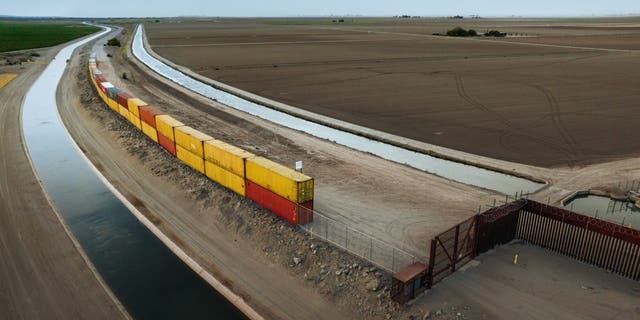 Aerial view of shipping containers being installed to fill gaps in the unfinished wall along the United States-Mexico border.