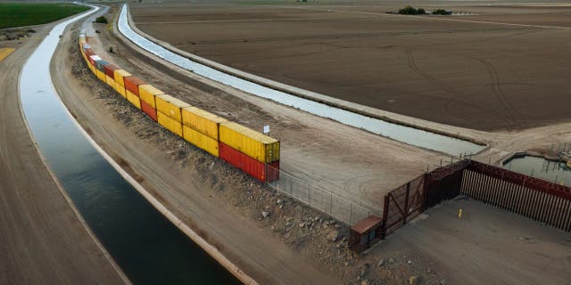 Aerial view of shipping containers being installed to fill gaps in the unfinished wall along the United States-Mexico border.