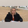 A woman with blonde hair sits at a table outside a courthouse.