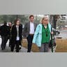 A group of people walk on a sidewalk, into a courthouse.