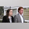 A man wearing a suit and a woman wearing a coat enter a courthouse.