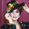 Gina Lollobrigida in a black hat with fruit on it and black shirt with colorful polka dots