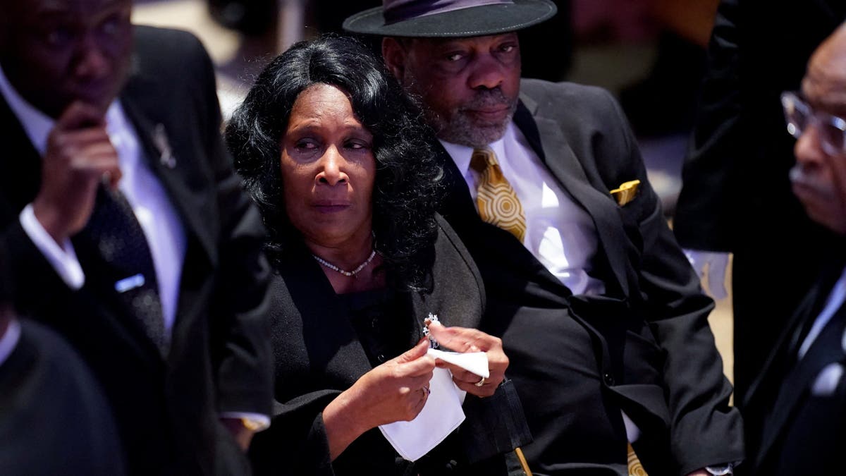 RowVaughn Wells in formal attire holding a tissue as she arrives at son's funeral