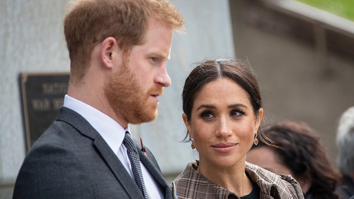 Meghan Markle looking serious while staring at a somber looking Prince Harry