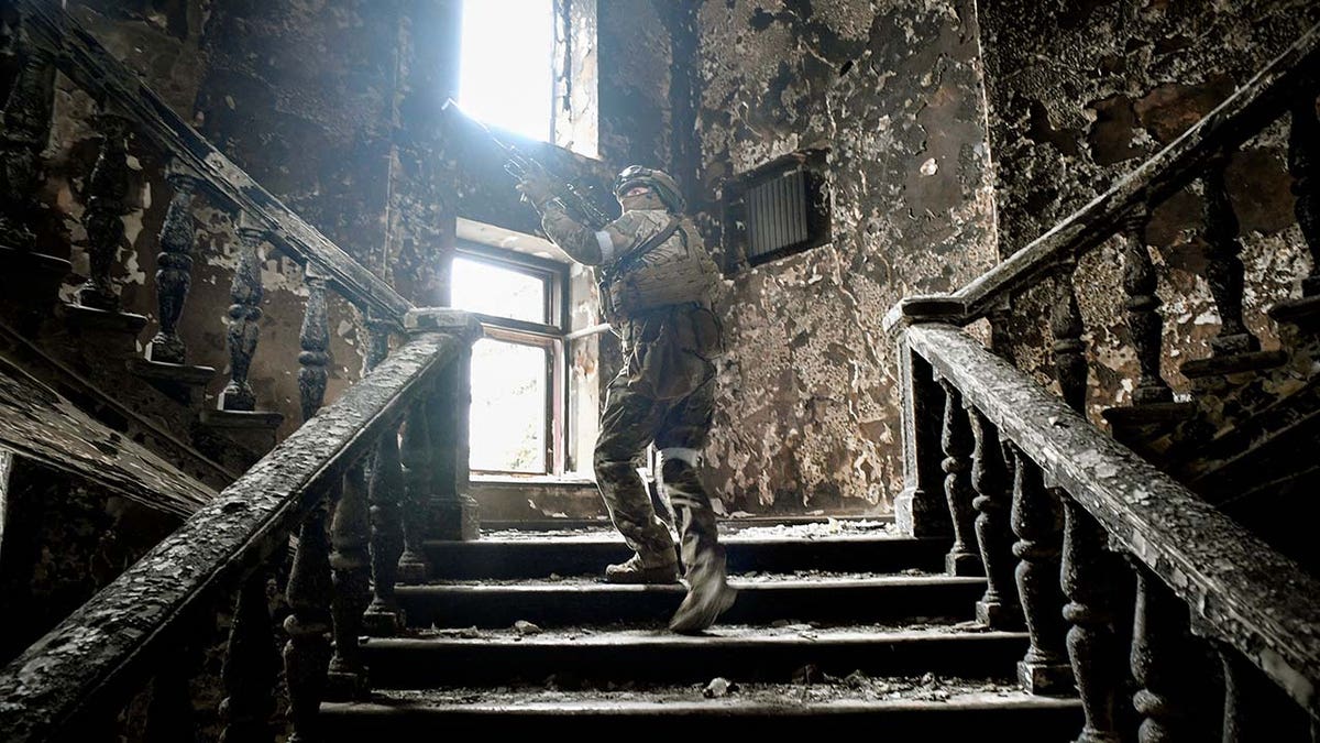 A soldier holding a gun walks up a destroyed staircase.