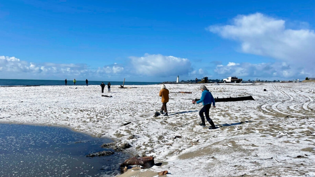 People walk along a snow-covered California beach