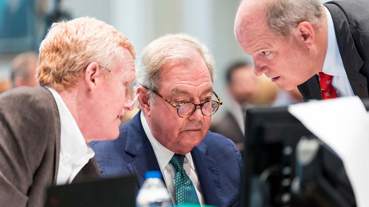 Three men speak inside a courtroom.