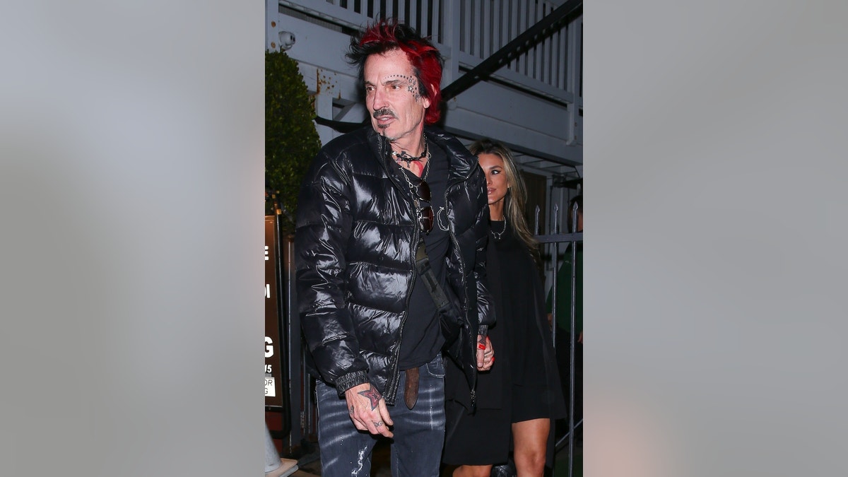 Tommy Lee, with face tattoo and red hair visible, walks in front of wife Brittany Furlan