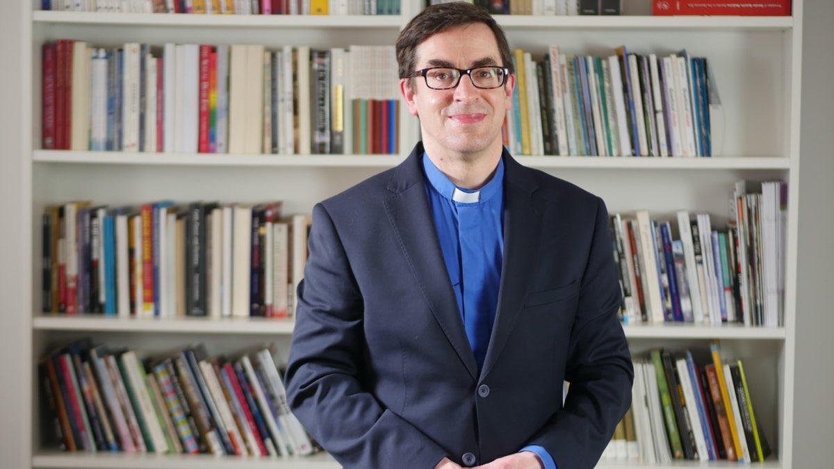 Rev. Dr. Bernard Randall in front of bookcase