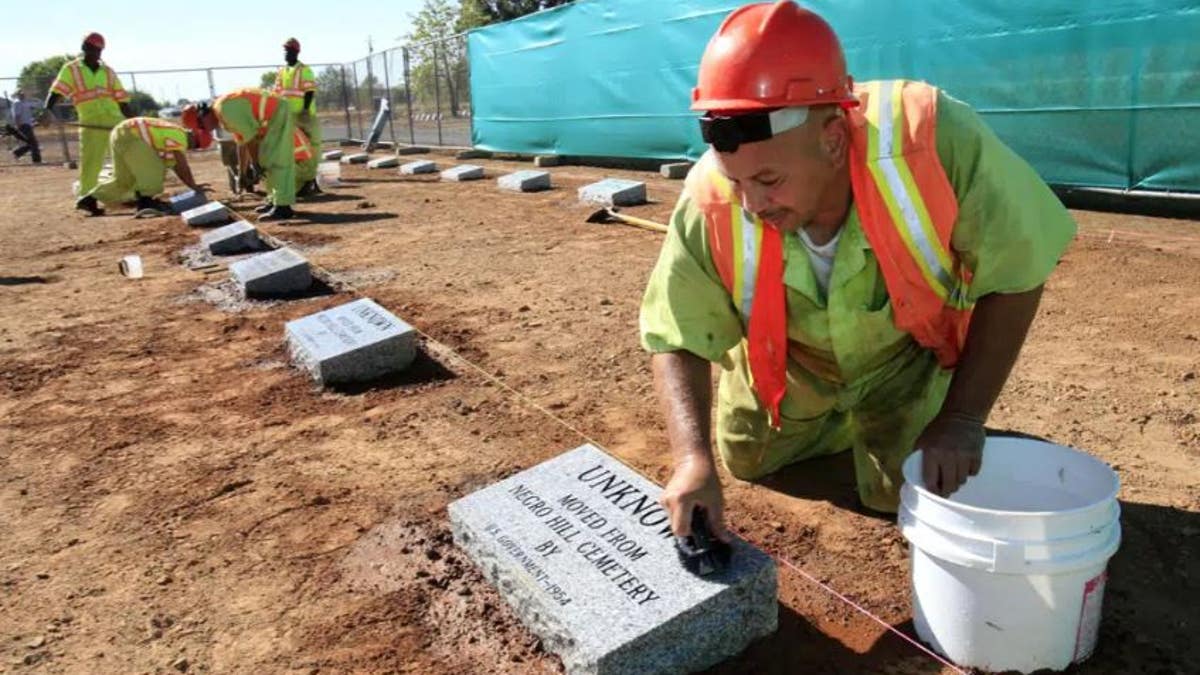 A California prisoner cleans a cemetery headstone