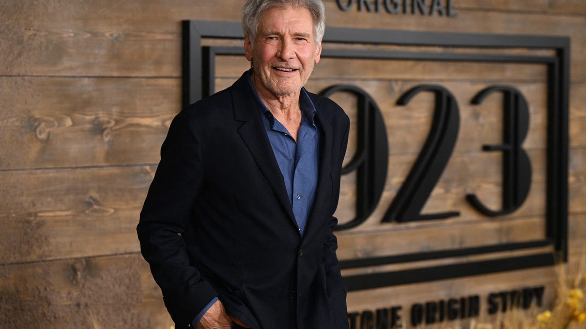 Harrison Ford smile in a black suit with a blue shirt a the premiere of "1923"