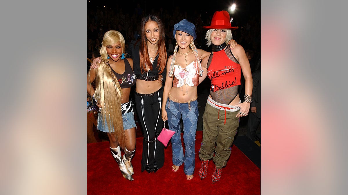 Lil' Kim in a crop top, jean skirt and zebra overlay next to Mya in a two-piece black outfit next to Christina Aguilera in jeans a busty crop top and jean hat next to Pink in a fishnet body suit, red tank top and hat and green pants at the 2001 MTV Video Muisc Awards