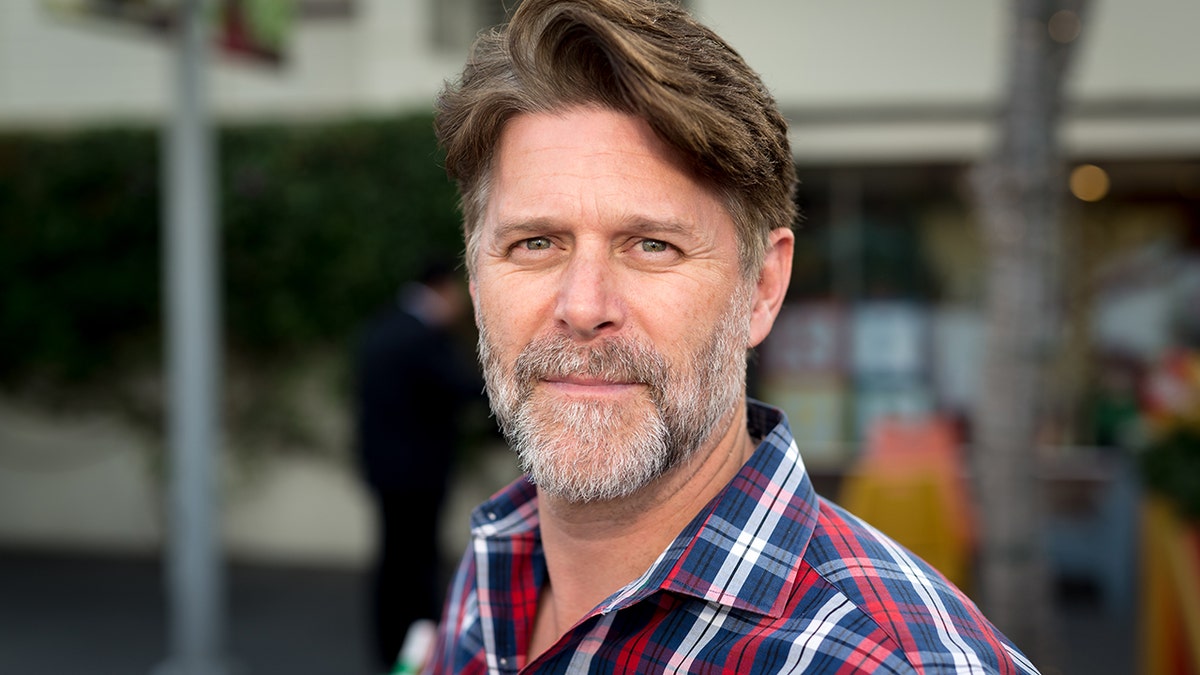 Slade Smiley in a red, white and blue plaid shirt soft smiles at the camera with graying beard